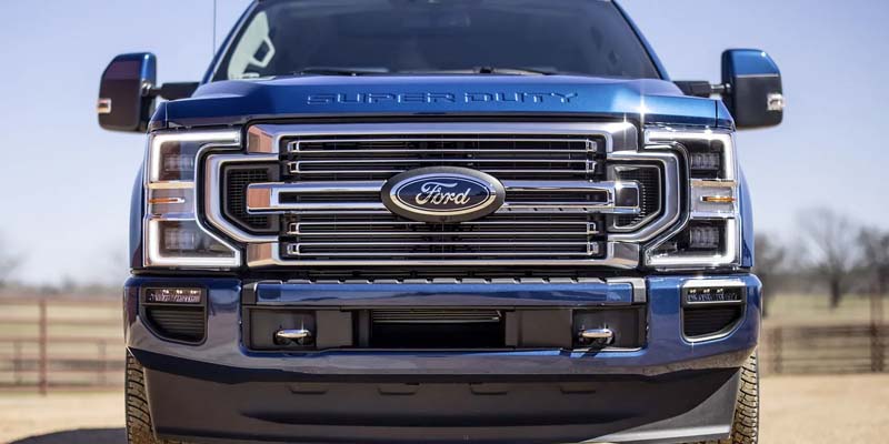 Front view of a blue Ford F-Series Super Duty truck, showing its large chrome grille and headlights.