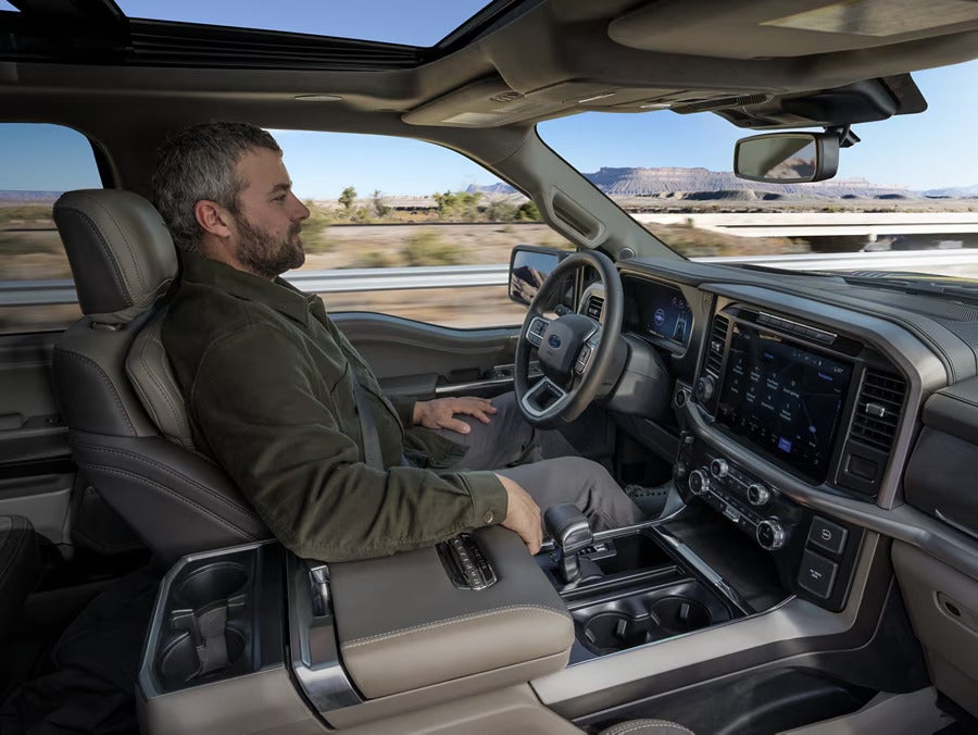 Man relaxes in a reclined car seat, with his hands placed on a flat console in front of him.