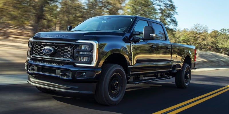 A black Ford F-Series Super Duty truck driving on a tree-lined road.